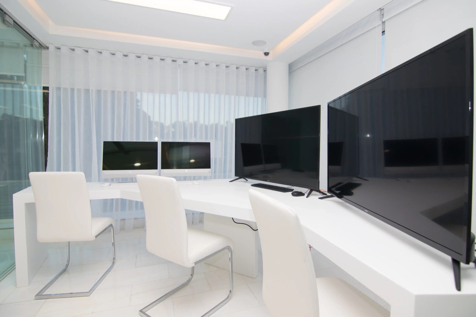 Bureaux blancs avec postes informatiques et grands écrans, voilages lumineux