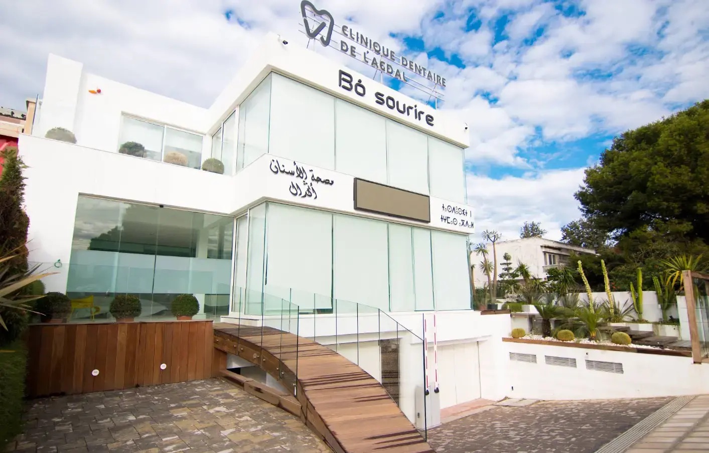 Façade blanche et vitrée de la clinique, enseigne Bô sourire et passerelle en bois