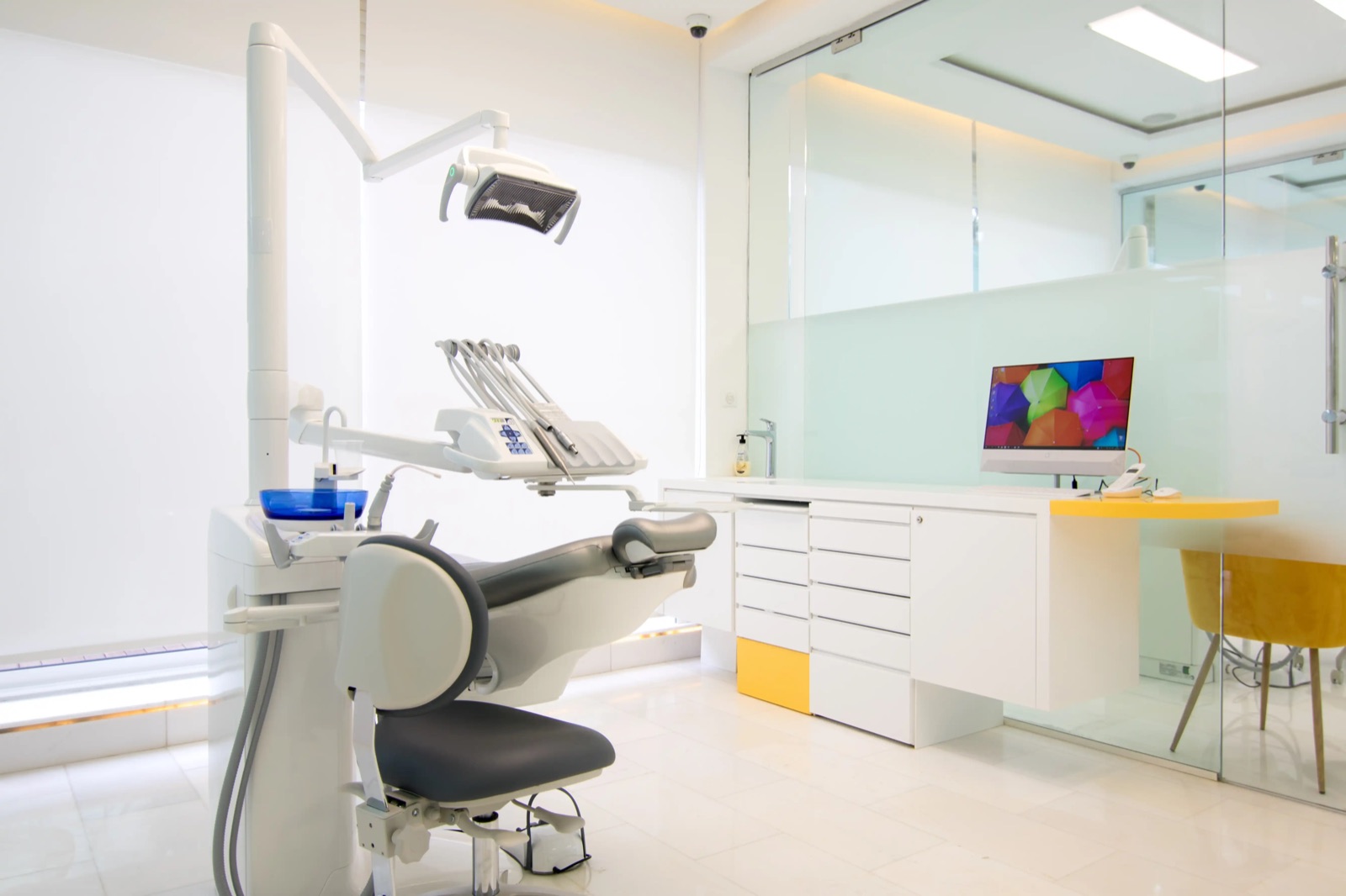 Salle de soins blanche avec fauteuil dentaire, mobilier blanc et touches jaunes